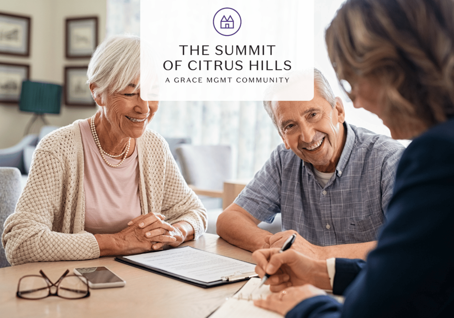 Smiling elderly couple signs paperwork with a community manager in a bright room; logo overlay reads The Summit of Citrus Hills.