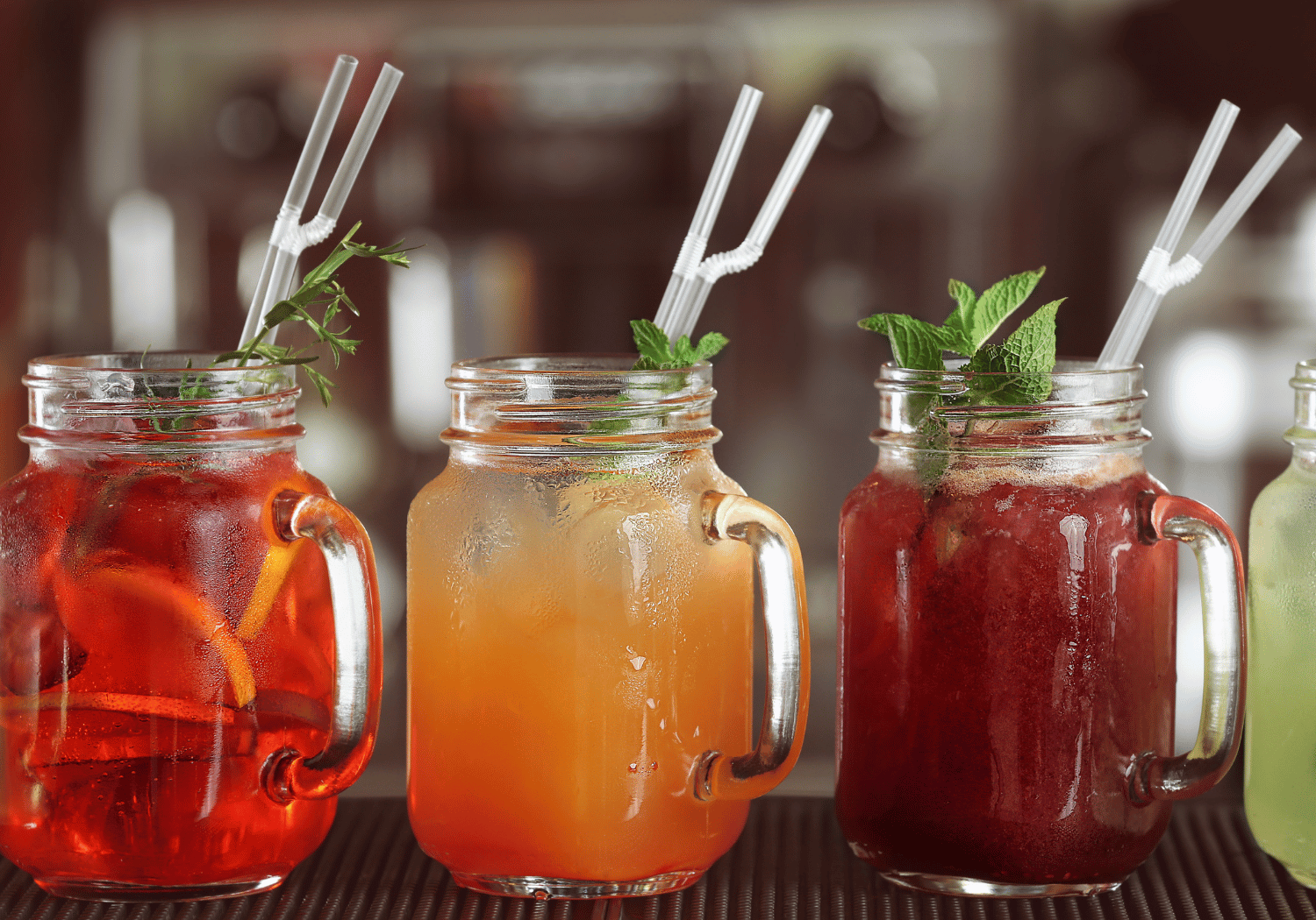 Three mason jar drinks with ice, citrus slices, and mint on a bar counter.